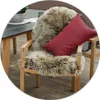 A sheepskin rug is draped over a wooden chair next to a table. Produktbild-Vorschau