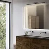 A modern bathroom vanity with a large mirror, sink, and faucet, illuminated by a sleek wall lamp. Anteprima dell’immagine prodotto