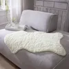 A fluffy beige faux fur rug is placed on a grey sofa, with a white tray holding a cup and a small vase of flowers on the sofa behind it. Produktbild-Vorschau