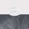 A white smoke detector is mounted on a white ceiling, with wisps of smoke visible below. Produktbild-Vorschau