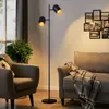 A floor lamp with two adjustable heads is placed between two armchairs in a living room setting. Produktbild-Vorschau