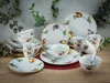 A collection of fruit-themed porcelain dinnerware is arranged on a wooden table with greenery in the background. Náhľad obrázku produktu