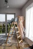 A room undergoing renovation with a ladder and furniture covered in plastic. Produktbild-Vorschau