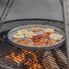 A round stainless steel grill plate filled with breakfast food, including pancakes, eggs, bacon, and hash browns, is placed over a fire on a grill. Podgląd zdjęcia produktu