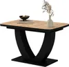 A dining table with a wood-look top and black base, decorated with a bowl of decorative orbs and a vase with dried flowers. Anteprima dell’immagine prodotto