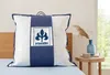 A pillow in its packaging is displayed on a bed, with a bedside table and vase in the background. Produktbild-Vorschau