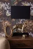 A close-up shot of a bedside table with a lamp, a golden animal figurine, and a picture frame against a floral wallpaper. Anteprima dell’immagine prodotto