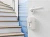 A white door handle and a white electronic lock device are mounted on a white wall next to a wooden staircase. Náhľad obrázku produktu