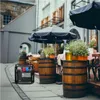 An inverter generator is placed on a cobblestone street next to outdoor seating at a cafe, with wooden barrels and potted plants. Produktbild-Vorschau