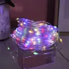 A coiled string of colorful LED lights sits on a clear acrylic box. Produktbild-Vorschau