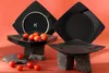 A set of black square plates with cherry tomatoes on them, arranged on rocks. Podgląd zdjęcia produktu