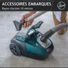 A person is using a green and gray Hoover vacuum cleaner on a carpeted floor. Produktbild-Vorschau