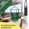 A green hanging chair with cushions is displayed on a wooden deck, with a green carrying bag and a black drink holder with a silver bottle shown as accessories. The background shows a balcony with furniture and a distant cityscape. Produktbild-Vorschau
