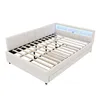 A white upholstered bed frame with a slatted mattress support and LED lighting in the headboard, shown from a diagonal angle against a white background. Náhled obrázku produktu