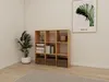 A wooden cube shelf unit filled with books and decorative items, placed in a room with a plant and a framed picture on the wall. Náhľad obrázku produktu