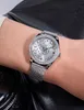 A close-up shot of a woman's wrist wearing a silver Guess watch with a diamond-encrusted bezel and a patterned dial. The background is black leather. Náhled obrázku produktu