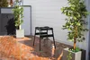 An outdoor patio with a black stand and a basket hanging from it, flanked by two potted trees. Anteprima dell’immagine prodotto