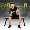 A man is sitting on a black weight bench and lifting a dumbbell. Náhľad obrázku produktu