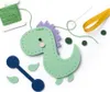 A felt dinosaur sewing kit laid out on a white background with various components. Produktbild-Vorschau
