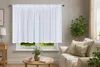 A white sheer curtain is hung over a window in a living room, with a sofa and a coffee table in the foreground. Produktbild-Vorschau
