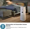 A bedroom scene with a person sleeping in bed and an air purifier in the foreground. Podgląd zdjęcia produktu