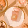 A perfume bottle is presented on a white plate, surrounded by pastries and a cup of coffee, in a warm, inviting setting. Voir les images du produit