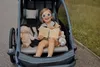 A young girl sits in a child trailer, holding a book. Produktbild-Vorschau