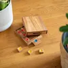 A wooden puzzle game with colored pieces is laid out on a wooden table, next to a potted plant. Produktbild-Vorschau