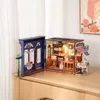Two miniature dollhouse kits, one resembling a blue storefront and the other a tea room, are displayed on a wooden surface. Produktbild-Vorschau