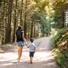 A woman and a child are walking on a dirt path through a forest. Produktbild-Vorschau
