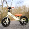 A balance bike for children is shown outdoors on a gravel path with trees in the background. Náhled obrázku produktu