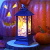 A Halloween-themed LED lantern sits on a wooden base, surrounded by pumpkins and autumn leaves. Produktbild-Vorschau