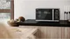 A black Sharp microwave with a grill function is displayed on a kitchen counter, next to a bowl of food and decorative candles. Anteprima dell’immagine prodotto