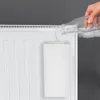 A hand is pouring water from a glass bottle into a white ceramic radiator humidifier attached to a white radiator. Produktbild-Vorschau