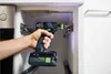 A person is using a cordless drill to attach a metal bracket inside a cabinet. Voir les images du produit