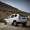 A white Dacia Duster SUV parked on a dirt road in a dry, hilly, desert-like environment. Produktbild-Vorschau