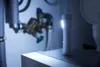 A white LED night light with a motion sensor is placed on a shelf next to plumbing fixtures in a dimly lit room. Produktbild-Vorschau