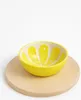 A yellow bowl with a lemon slice design sits on a wooden cutting board against a white background. Voir les images du produit