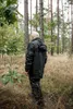 A person wearing a black rain suit stands in a forest. Produktbild-Vorschau