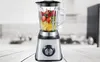 A blender filled with fruit sits on a wooden table in a kitchen setting. Produktbild-Vorschau