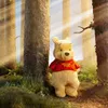Winnie the Pooh plush toy standing in a forest setting with sunlight filtering through the trees. Produktbild-Vorschau