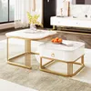 A modern living room setting with two marble-look coffee tables, one larger and one smaller, placed on a rug. The larger table has books and a vase with yellow flowers, while the smaller table has a drawer and a bowl of oranges. Voir les images du produit