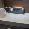 A power strip with multiple outlets is shown on a white countertop, with a mug and a kettle in the background. Produktbild-Vorschau