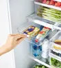 A hand is pulling a clear plastic drawer out of a refrigerator. The drawer contains a package of butter and a tube of jam. Produktbild-Vorschau