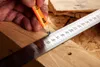 A close-up shot of a hand using a pencil and a metal ruler to mark a wooden plank. Podgląd zdjęcia produktu