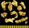 A collection of gold nuggets on a black background with a ruler at the bottom. Produktbild-Vorschau