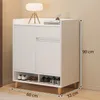 A white shoe cabinet with wooden legs, decorated with a lamp and books on top, and shoes on the shelves below. Náhľad obrázku produktu