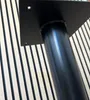 A close-up of a black metal table base with a square mounting plate, set against a background of light-colored wooden slats with dark vertical stripes. Náhled obrázku produktu