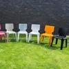Several colorful plastic chairs are lined up on a green lawn in front of a brick wall. Produktbild-Vorschau