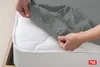 A person's hands are shown stretching a gray fitted sheet over a white mattress. Produktbild-Vorschau